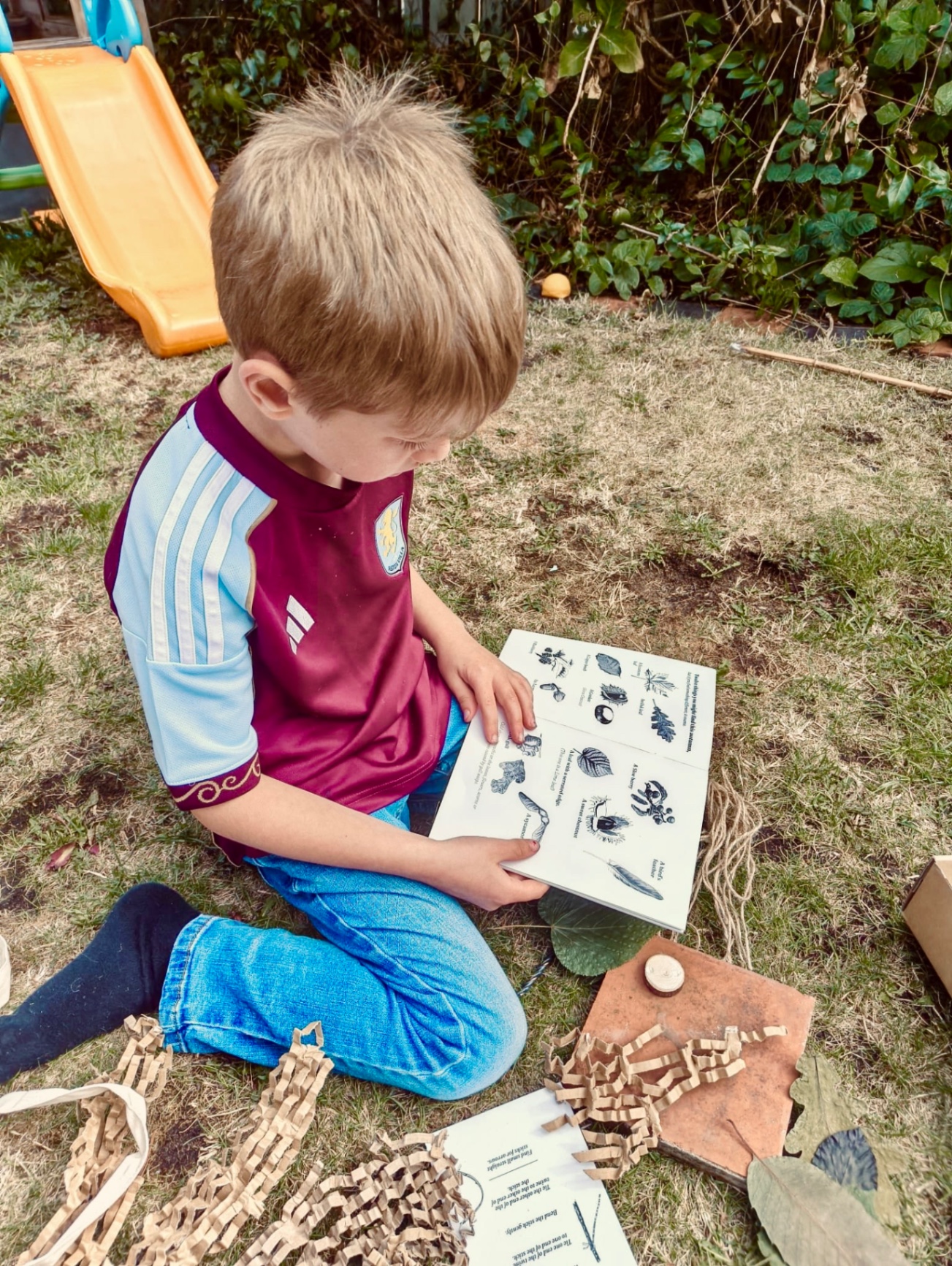 A child sitting in the garden, looking at the forager's illustrated notebook